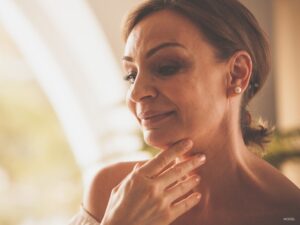 mature woman touching her neck meant to represent a person considering neck lift surgery